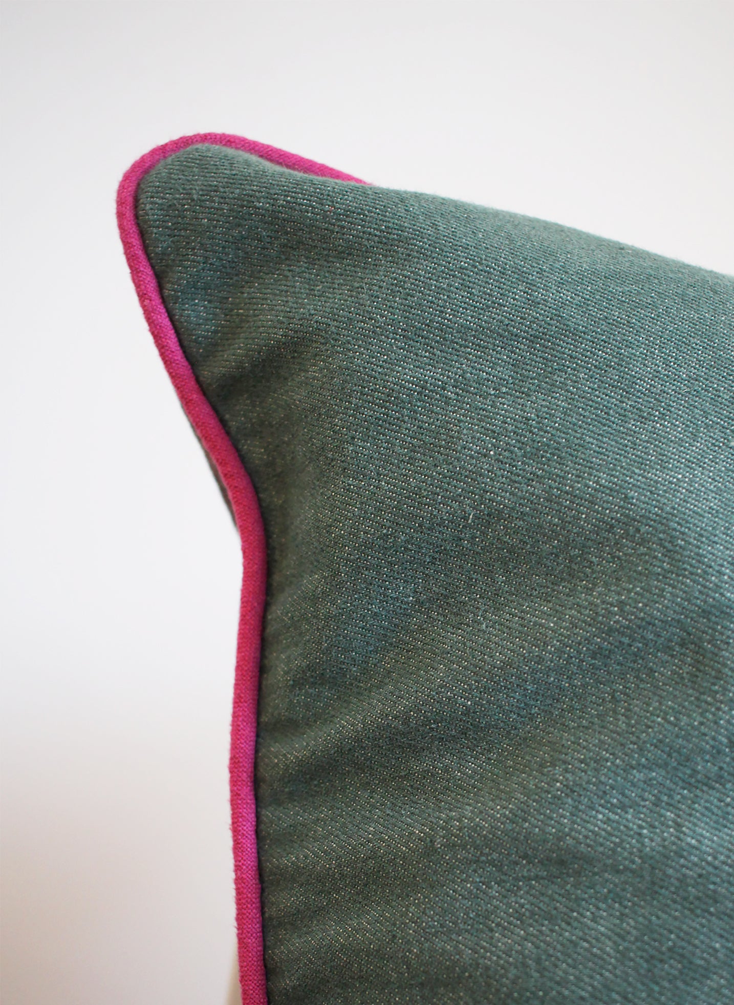 Corner of green denim cushion and pink piping
